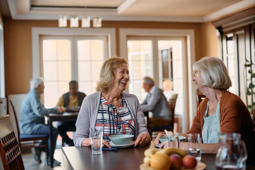 Elderly women laughing and having coffee in rest home