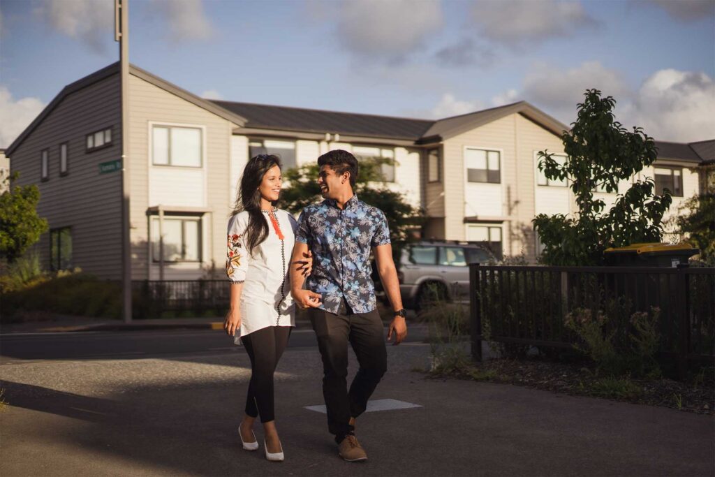 Young couple holding hands outside house smiling and walking