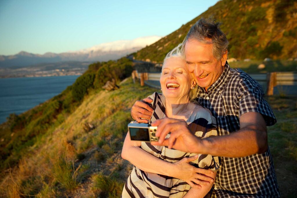 Older couple laughing at sunset taking selfie