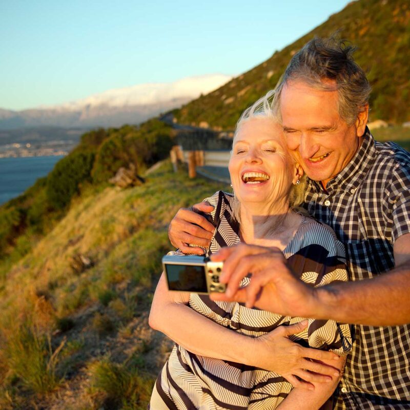 Older couple laughing at sunset taking selfie
